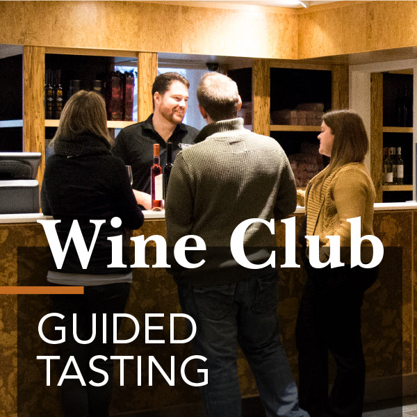 Members of a wine club gathered at a bar, with a man serving wine to a woman, while another woman talks on the phone. The background displays a wine list on the wall.